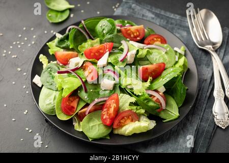 Gesunder Gemüsesalat aus frischem Gemüse aus Tomaten, Spinat, Salat und Sesam auf einem Teller. Nützliche Ernährung. Stockfoto