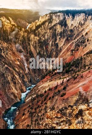 Tiefer Canyon mit farbenfrohen orangefarbenen, roten und gelben Wänden, frühmorgendlicher Sonnenaufgang und tief am unteren Rand des Canyons mit grünem Wald auf Höhe von m. Stockfoto