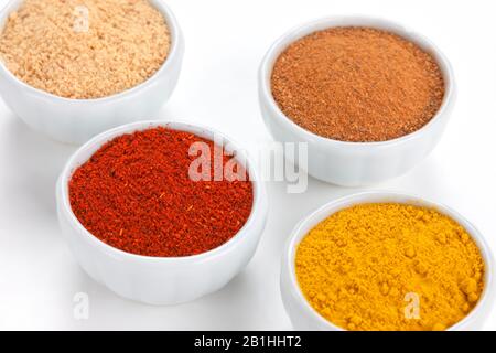 Verschiedene Gewürze in weißen Schüsseln isoliert auf weißem Hintergrund. Paprika, Curry, Black Pepper, Ginger, Cinnamon, Bay Leaves. Stockfoto