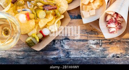 Tapas- und Pinchos-Panorama, aufgenommen von oben mit Kopierbereich. Käse, Jamon und Oliven, gildas und Kartoffelchips, mit Wein, auf einem Holztisch Stockfoto