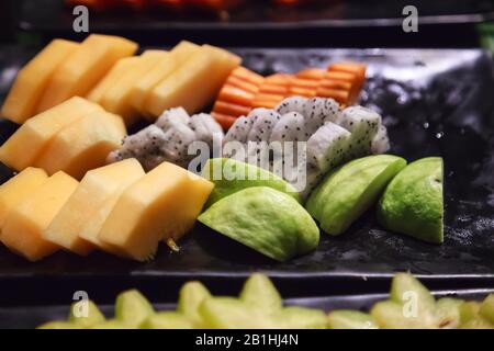 Frische, verschiedene tropische asiatische saisonale Früchte (Guava, Drachenfrucht, Papaya, Kantaloupe) in schwarzem Tablett. Vegetarische und vegetarische Speisen, Natürliche und Stockfoto