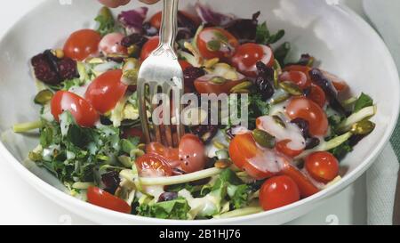 Gemüsesalat aus grünen Blättern, Tomaten, Kürbissamen, getrockneten Preiselbeeren und Dressing auf einem Teller in der Nähe. Stockfoto