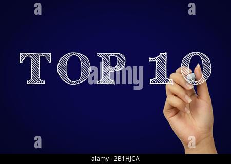 Weibliche Hand schreibt Top Ten Text mit weißem Kreidestift in kreativem Doodle-Stil - Top 10 handgezeichnete Kopie mit dunkelmarineblauem Gradientenhintergrund - Produktpreise, Reisebewertung und Wettbewerbskonzept Stockfoto