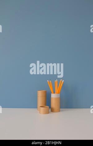 Papierröhrchen mit gelben Bleistiften auf weißem Tisch auf blauem Hintergrund. Recycling-Konzept, das zeigt, wie Papierrohre zu Hause oder im Büro wiederverwendet werden Stockfoto