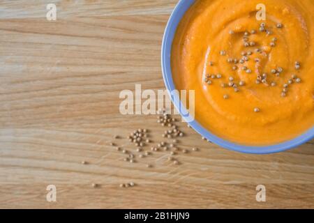 Draufsicht auf Kürbis und Karottensuppe in blauer Schüssel auf Holzhintergrund mit Koriander mit Kopierraum Stockfoto