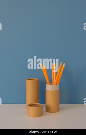 Papierröhrchen mit gelben Bleistiften auf weißem Tisch auf blauem Hintergrund. Recycling-Konzept, das zeigt, wie Papierrohre zu Hause oder im Büro wiederverwendet werden. Kopierbereich Stockfoto