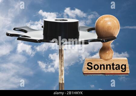 Ein Stempel mit der Aufschrift Sonntag (Sonntag) hängt in einer Stempelablage, Hintergrundhimmel Stockfoto