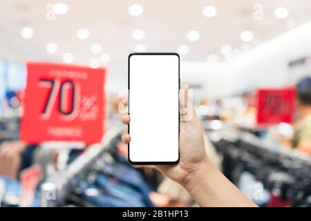 Abstraktes Mockup-Handy mit verschwommenem Bekleidungsgeschäft und Rabattschild. Verstauen Sie Ihr Smartphone im Einzelhandel, und sparen Sie 70 % im Innenbereich Stockfoto