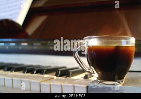 Tasse heißen Kaffee mit Rauch und verschwommener Klaviertastatur im Hintergrund Stockfoto