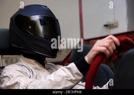 Ein Profi-Rennfahrer in einem schwarzen Helm und einem weißen Homologieranzug sitzt auf dem Sportsitz eines Autos zum Driften und Rennen während eines Rennens und Trainins Stockfoto