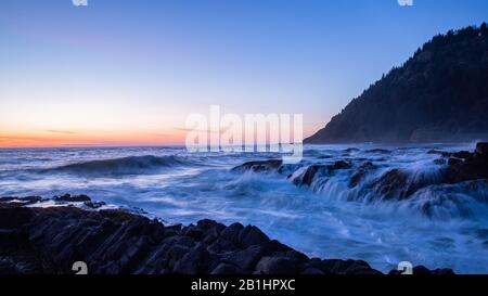 Sonnenuntergang über dem Pazifischen Ozean. Foto mit langer Belichtung von abstürzenden Wellen. Seidiges Wasser, das in Basaltfelsen in der Nähe von Cape Perpetua, Oregon, in eine Passage eindringt Stockfoto