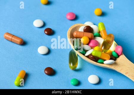 Holzlöffel voller Pillen, Tabletten, Vitamine, Medikamente, Omega-3-Fischöl, Gelkapseln, Medikamente und Nahrungsergänzungsmittel für die Gesundheit. Blauer Hintergrund. Stockfoto