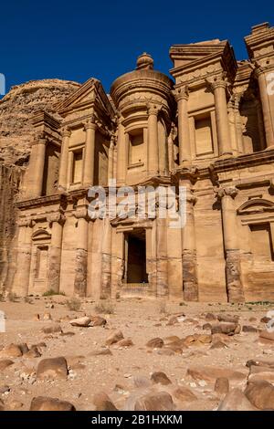 Sonniger, wolkenloser Tag, felsiger Vordergrundblick auf den atemberaubenden Ad-Deir in der antiken Stadt Petra, Jordanien. Ad-Deir oder Das Kloster. Petra Komplex und Touristenattraktion, Haschemite Königreich Jordanien Stockfoto