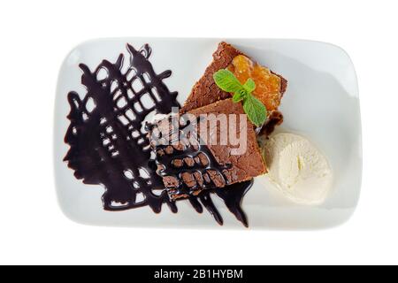 Schokoladenkuchen braun auf weißem Teller mit Aprikose, Pfirsichmarmelade, Minze, Belag und Vanilleeis isoliert auf weißem Hintergrund. Dessert für ein Menü Stockfoto