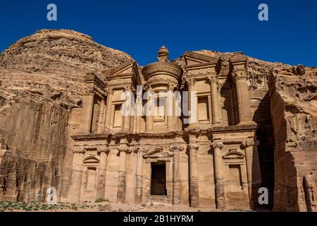 Sonniger, wolkenloser Tag, felsiger Vordergrundblick auf den atemberaubenden Ad-Deir in der antiken Stadt Petra, Jordanien. Ad-Deir oder Das Kloster. Petra Komplex und Touristenattraktion, Haschemite Königreich Jordanien Stockfoto