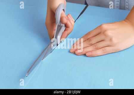 Schere, die blaues Material schneidet. Nahaufnahme der Hände eines jungen Mädchens Näherin, das Stoff schneidet Stockfoto