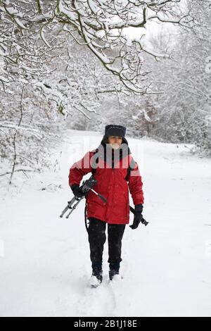 Weibliche Fotografin, die im Winter ein Stativ durch eine schneebedeckte Landschaft tragen Stockfoto