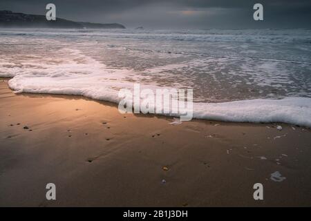 Abendlicht, während eine sanfte Welle auf einer ankommenden Flut an einem kalt kühlt windigen Fistral Beach in Newquay in Cornwall strömt. Stockfoto