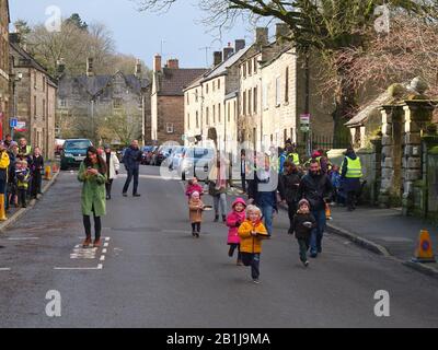 Kleinkinder Rennen auf der Hauptstraße des Dorfes mit Pfannen und Pfannkuchen während Winster Pancake-Rennen am Dienstag Shrove Pancake Day Derbyshire UK Stockfoto