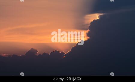 Lauernd gelb-oranger Sonnenuntergang hinter den Wolken. Hell beleuchteter Umriss der Wolken. Stockfoto