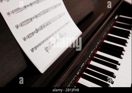 Musiknotizbuch mit Musikstück und Geigenschlüssel auf einem Ständer für ein elektrisches Klavier mit weißen Tasten. Lernen, Klavier zu spielen. Stockfoto