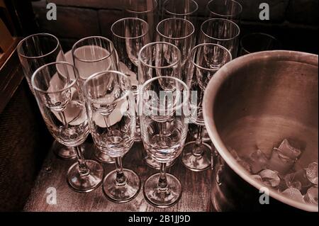 Viele identische leere Sektgläser auf dem Tisch, neben einem Eiseimer aus Metall für Getränke Stockfoto