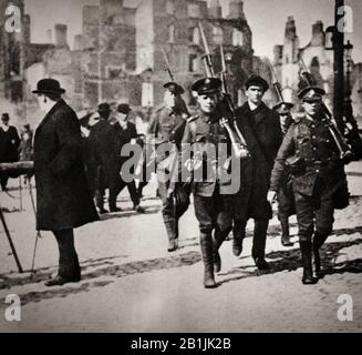 Ein irischer Nationalist wird von britischen Oldiern nach dem Osteraufstand von 1916, einem bewaffneten Aufstand in Irland während der Osterwoche, April 1916, unter Begleitung nach Dublin Castle geführt. Sie wurde von den irischen republikanern ins Leben gerufen, um die britische Herrschaft in Irland zu beenden und eine unabhängige irische Republik zu gründen, während das Vereinigte Königreich den Ersten Weltkrieg bekämpfte. Es war die erste bewaffnete Aktion der irischen Revolutionsperiode. Sechzehn der Anführer Der Aufstiege wurden im Mai 1916 hingerichtet, aber nachfolgende politische Entwicklungen trugen letztlich zur irischen Unabhängigkeit bei. Stockfoto