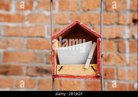 Ein Holzhaus mit Papier für Notizen im Inneren, mit einer Wäscheklammer vor dem Hintergrund einer Ziegelmauer auf der Straße befestigt. Art Objekt die Fähigkeit t Stockfoto