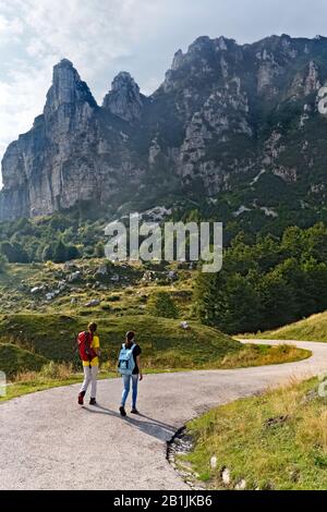Zwei Wanderer gehen in Campogrosso vorbei. Im Hintergrund Mount La Sisilla. Piccole Dolmiti, Provinz Vicenza, Venetien, Italien, Europa. Stockfoto
