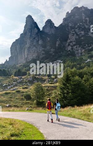 Zwei Wanderer gehen in Campogrosso vorbei. Im Hintergrund Mount La Sisilla. Piccole Dolmiti, Provinz Vicenza, Venetien, Italien, Europa. Stockfoto