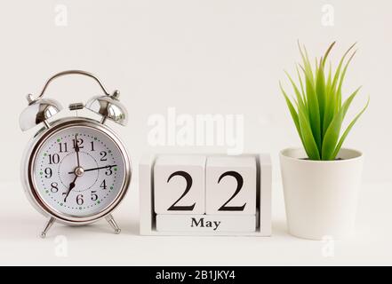 22. Mai auf einem Holzkalender neben einem Wecker und einer Blume. Ein Tag des Frühlingsmonats, Kalender und Wecker auf hellem Hintergrund. Frühling i Stockfoto