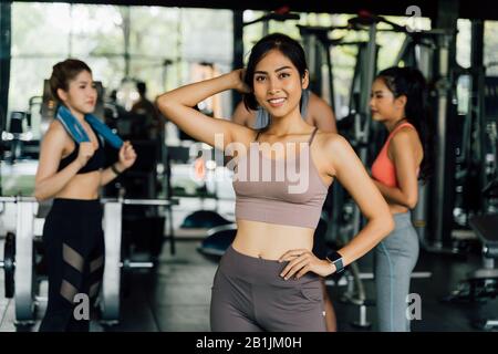 Fröhliche junge, gesunde asiatische Trainerin, die im Fitnessstudio mit multirassischen Freunden auf die Kamera blickt Stockfoto