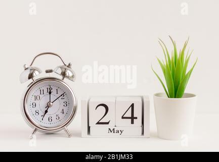 24. Mai auf einem Holzkalender neben einem Wecker und einer Blume. Ein Tag des Frühlingsmonats, Kalender und Wecker auf hellem Hintergrund. Frühling i Stockfoto