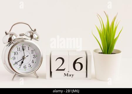 26. Mai auf einem Holzkalender neben einem Wecker und einer Blume. Ein Tag des Frühlingsmonats, Kalender und Wecker auf hellem Hintergrund. Frühling i Stockfoto