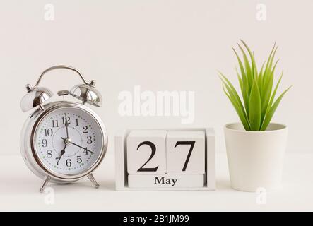 27. Mai auf einem Holzkalender neben einem Wecker und einer Blume. Ein Tag des Frühlingsmonats, Kalender und Wecker auf hellem Hintergrund. Frühling i Stockfoto