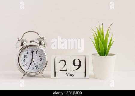 29. Mai auf einem Holzkalender neben einem Wecker und einer Blume. Ein Tag des Frühlingsmonats, Kalender und Wecker auf hellem Hintergrund. Frühling i Stockfoto