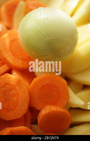 Rohe Zwiebeln und runde Karotten- und Kartoffelscheiben liegen dicht beieinander. Gemüseset für Suppe. Gesundes veganes Essen. Stockfoto