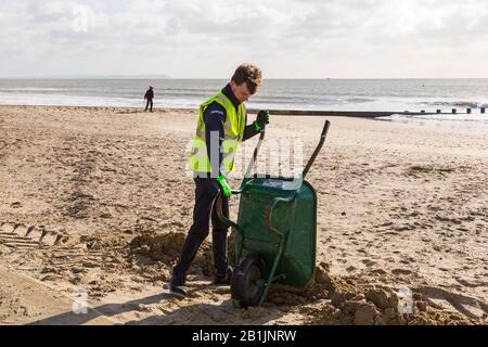 Bournemouth, Dorset, Großbritannien. Februar 2020. Stadtrat Lewis Allison bleibt stecken und gibt den Rangern am Meer eine Hand, um den Sand von der Promenade zu entfernen, der von den jüngsten starken Winden und dem Sturm Dennis geblasen wurde. Stadtrat Allison ist Labour-Ratsherr für Boscombe West und Portfolio-Inhaber, Kabinettsmitglied, für Tourismus, Freizeit und Gemeinden im BCP-Rat (Bournemouth, Christchurch und Poole). Credit: Carolyn Jenkins/Alamy Live News Stockfoto