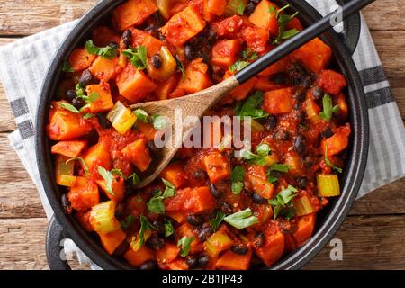 Leckere würzige Süßkartoffeln und schwarze Bohnen mit Tomaten in einer Pfanne auf dem Tisch. Horizontale Draufsicht von oben Stockfoto