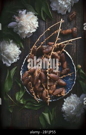 Keramikschale mit vielen Datteln auf rustikaler Holztischoberfläche mit weißen Blumen Stockfoto