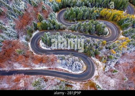 Luftbild einer kurvenreichen Bergstraße, die durch einen Tannenwald führt. Winter mit Schnee Stockfoto