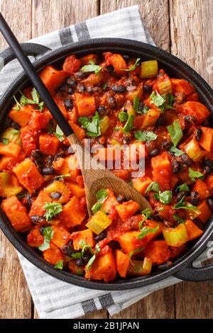 Gebratene Chili Süßkartoffeln und schwarze Bohnen mit Tomaten, Sellerie in einer Pfanne auf dem Tisch. Vertikale Draufsicht von oben Stockfoto