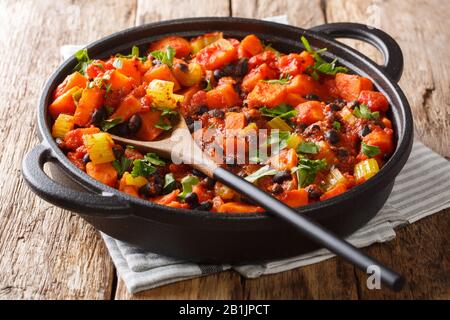 Traditionelles Rezept für Chili Süßkartoffeln und schwarze Bohnen mit Tomaten, Sellerie in einer Pfanne auf dem Tisch. Horizontal Stockfoto
