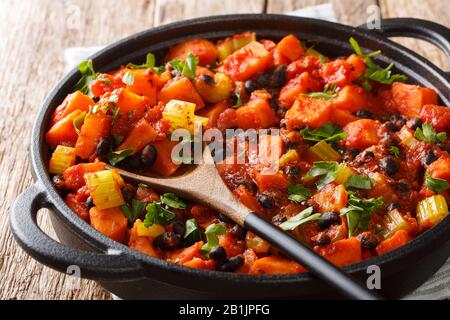 Chili Süßkartoffeln und schwarze Bohnen mit Tomaten, Sellerie in einer Pfanne auf dem Tisch. Horizontal Stockfoto