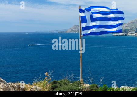 Schöne mediterrane Landschaft mit einer griechischen Flagge, die an einem sonnigen Tag im Wind fliegt (Rhodos, Griechenland) Stockfoto