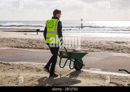 Bournemouth, Dorset, Großbritannien. Februar 2020. Stadtrat Lewis Allison bleibt stecken und gibt den Rangern am Meer eine Hand, um den Sand von der Promenade zu entfernen, der von den jüngsten starken Winden und dem Sturm Dennis geblasen wurde. Stadtrat Allison ist Labour-Ratsherr für Boscombe West und Portfolio-Inhaber, Kabinettsmitglied, für Tourismus, Freizeit und Gemeinden im BCP-Rat (Bournemouth, Christchurch und Poole). Credit: Carolyn Jenkins/Alamy Live News Stockfoto