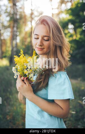 Das Mädchen hält Wildblumen in den Händen. Mädchen spaziert bei Sonnenuntergang im Wald Stockfoto