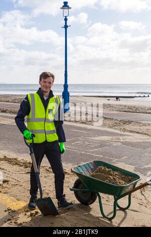 Bournemouth, Dorset, Großbritannien. Februar 2020. Stadtrat Lewis Allison bleibt stecken und gibt den Rangern am Meer eine Hand, um den Sand von der Promenade zu entfernen, der von den jüngsten starken Winden und dem Sturm Dennis geblasen wurde. Stadtrat Allison ist Labour-Ratsherr für Boscombe West und Portfolio-Inhaber, Kabinettsmitglied, für Tourismus, Freizeit und Gemeinden im BCP-Rat (Bournemouth, Christchurch und Poole). Credit: Carolyn Jenkins/Alamy Live News Stockfoto