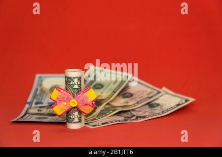 Dollar mit einem festlichen Bogen verbunden. Amerikanische Währung, Geldscheine aus Papier. Ständiger Kalender mit Holzwürfeln. Geburtstag des Dollars feiern Stockfoto