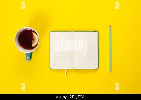 Mint Tea Tasse und schickes Notizbuch mit leerer oder leerer Seite auf hellgelbem Schreibtisch von oben, Planung und Designkonzept. Draufsicht, flaches Layout, Kopierbereich Stockfoto